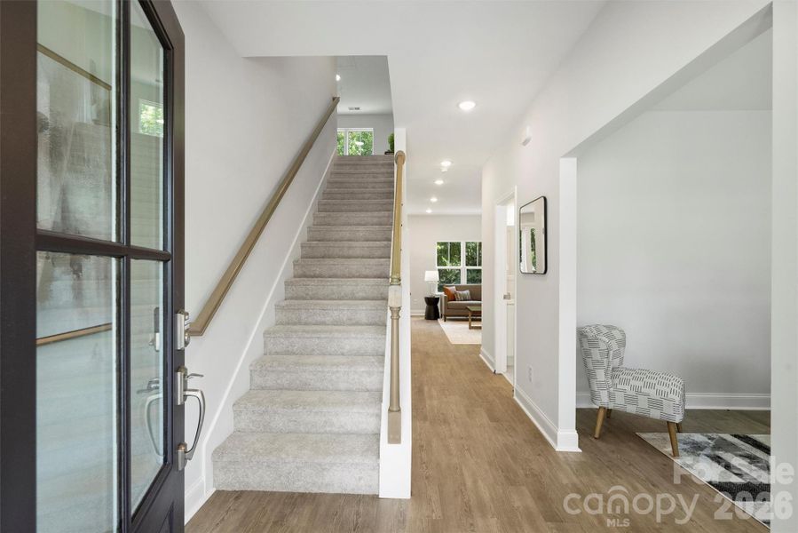Light filled entry with glass front door, staircase, and sightlines through the home to the main living area.
