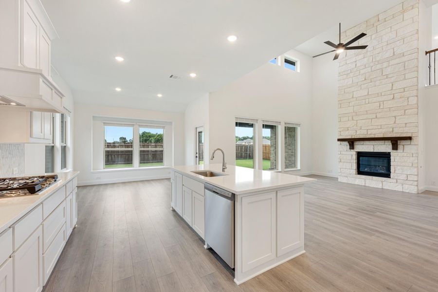 Open-concept kitchen with white island, stone fireplace, vaulted ceiling, and light wood floors