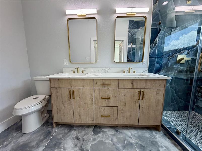 Double vanity featuring a wood-finish cabinet with gold-toned hardware, dual rectangular mirrors with gold frames, and white countertops Double vanity featuring a wood-finish cabinet with gold-toned hardware, dual rectangular mirrors with gold frames, and white countertops
