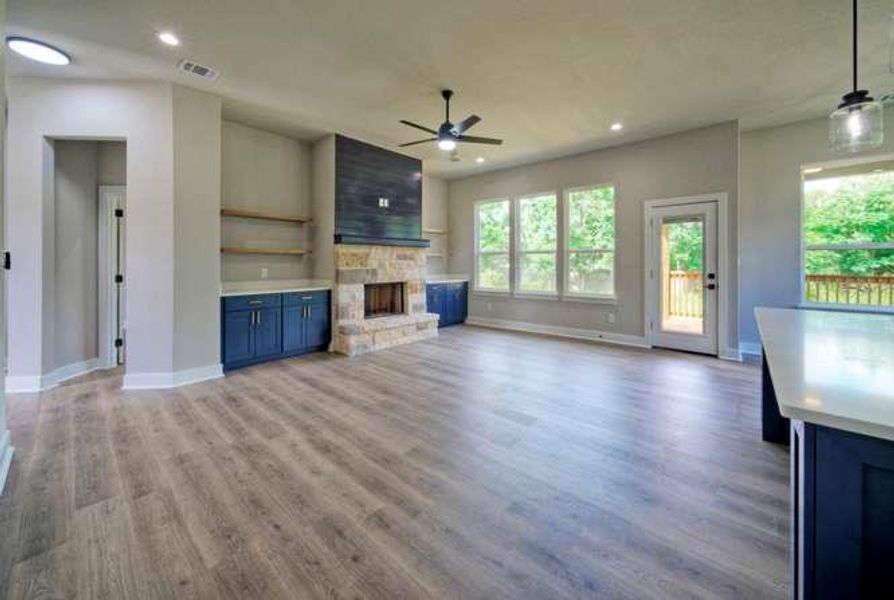 A spacious living area features a stone fireplace, built-in cabinetry, and wide plank flooring.