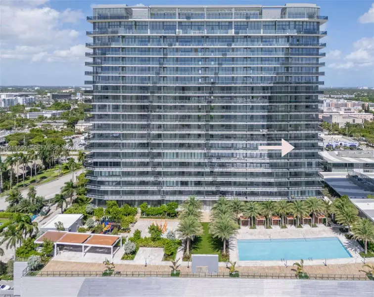 High-rise architectural exterior featuring glass-paneled balconies, a ground-level swimming pool, hardscaped patio, integrated landscaping, and covered cabanas