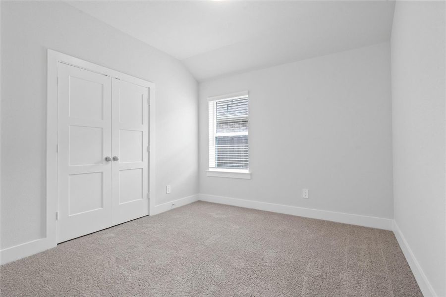 This inviting secondary bedroom combines comfort and modern elegance, featuring plush carpeting, a neutral color palette, closet, and abundant natural light streaming through a large window (fitted with blinds).