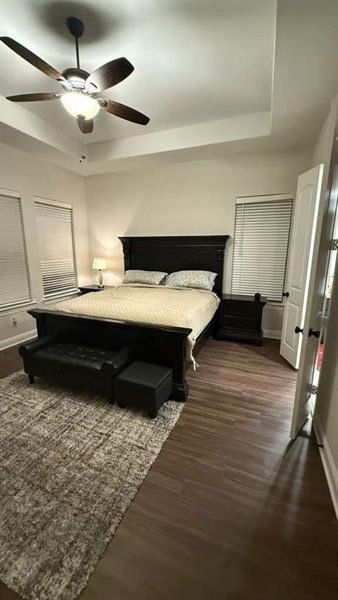 Bedroom with a raised ceiling, dark wood-style flooring, and a ceiling fan