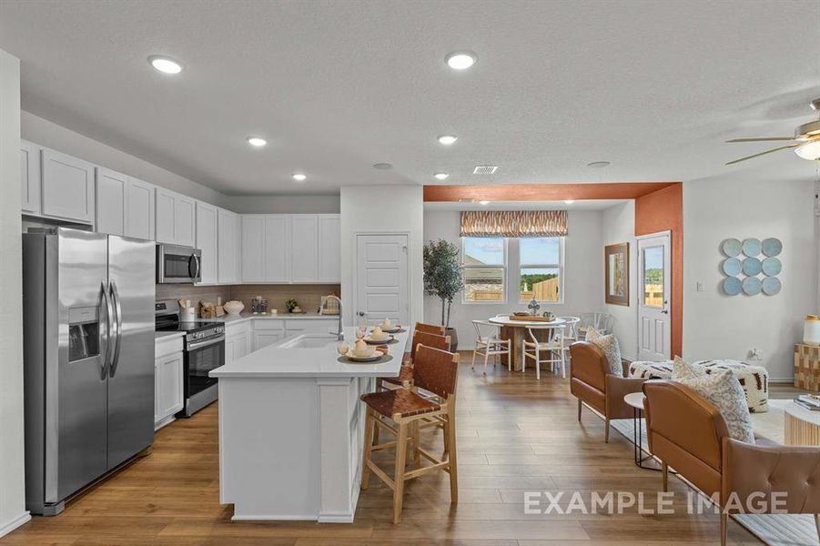 Kitchen with tasteful backsplash, stainless steel appliances, sink, white cabinetry, and an island with sink