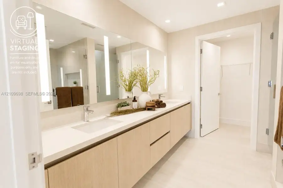 Full-width vanity featuring light wood-finish cabinetry, dual undermount sinks, solid-surface countertops, recessed lighting, and wall-mounted vertical vanity mirrors with integrated illumination