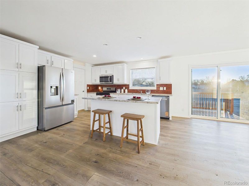 This crisp white kitchen includes ample cabinet storage, stainless steel fridge, and access to the back deck—combining style with convenience.