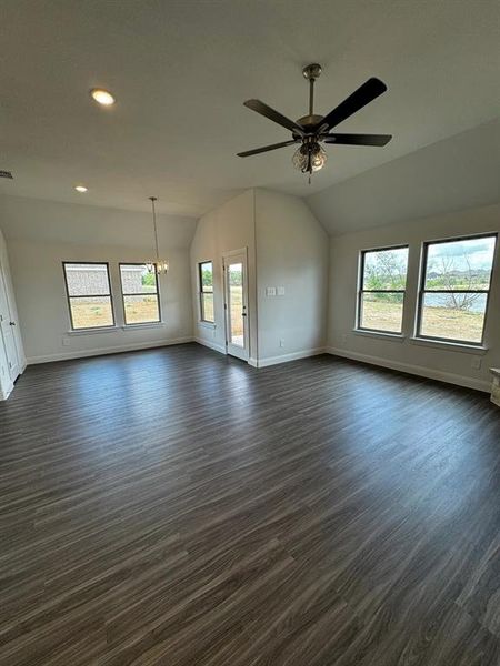 Unfurnished living room featuring ceiling fan with notable chandelier, lofted ceiling, and dark wood-type flooring