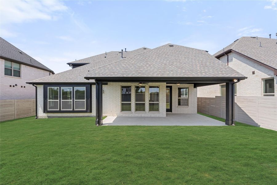Back of single-story brick home with covered patio, large windows, and green lawn Back of single-story brick home with covered patio, large windows, and green lawn