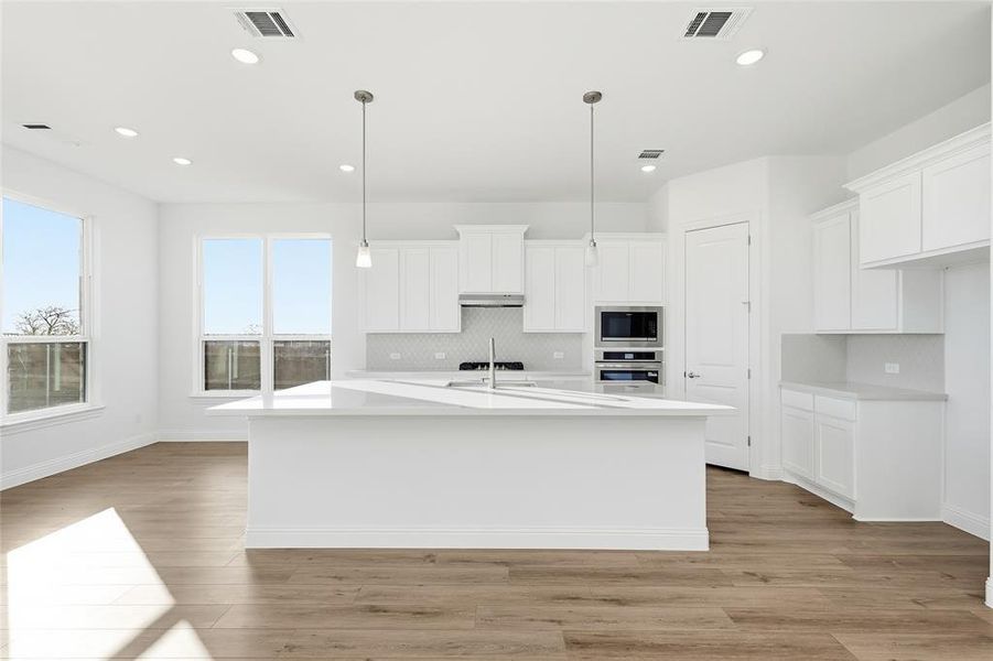 Kitchen featuring white cabinets, an island with sink, light wood-style floors, stainless steel appliances, and tasteful backsplash Kitchen featuring white cabinets, an island with sink, light wood-style floors, stainless steel appliances, and tasteful backsplash
