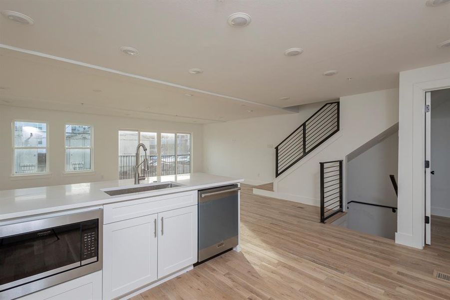 Kitchen with light wood-style flooring, stainless steel appliances, a sink, white cabinetry, and light countertops