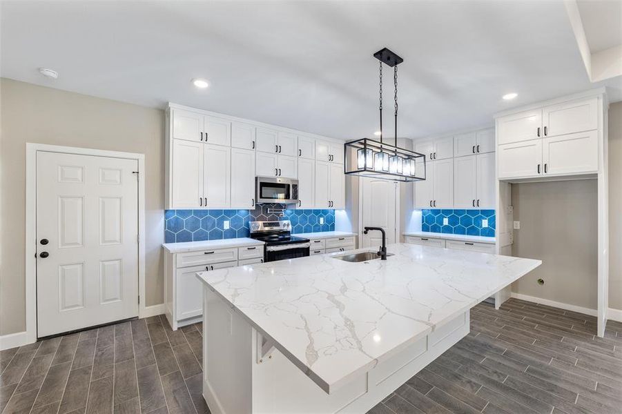 Kitchen with sink, appliances with stainless steel finishes, a kitchen island with sink, white cabinetry, and decorative light fixtures