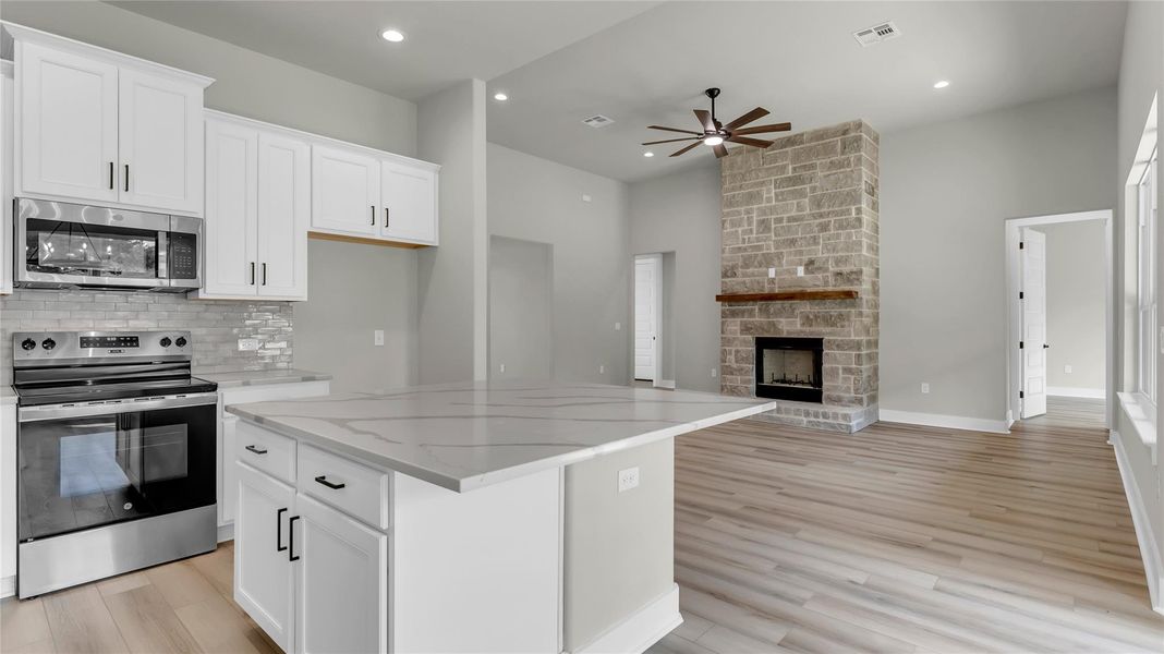 Kitchen featuring stainless steel appliances, white cabinetry, a center island, light wood-style floors, and a stone fireplace