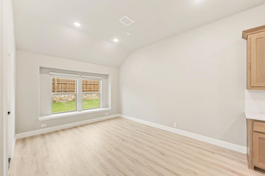Empty room with vaulted ceiling, light wood floors, and a window overlooking a backyard Empty room with vaulted ceiling, light wood floors, and a window overlooking a backyard