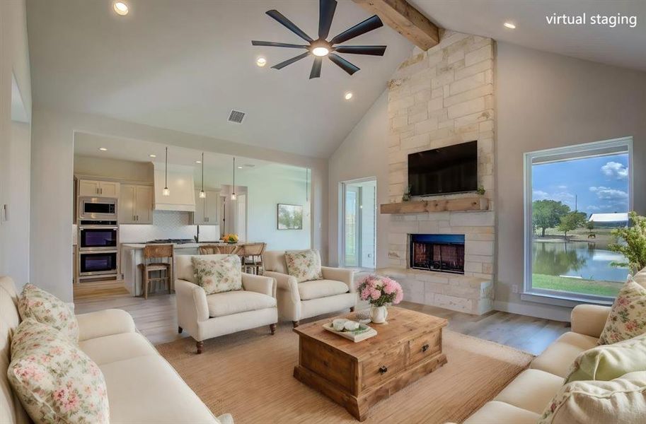 Living room featuring a water view, high vaulted ceiling, beamed ceiling, light hardwood / wood-style floors, and a stone fireplace