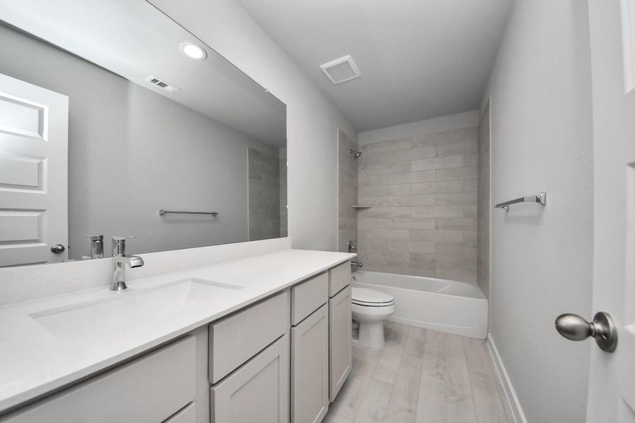 Secondary bath features tile flooring, bath/shower combo with tile surround, light stained wood cabinets, beautiful light countertop. Sample photo of completed home with similar floor plan. Actual colors and selections may vary.