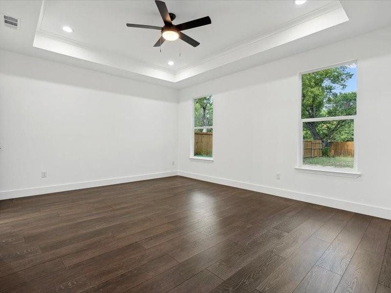 Empty room with a tray ceiling, dark wood-type flooring, and ceiling fan