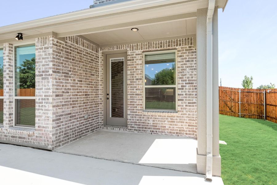 Covered back patio with concrete slab, brick exterior, rear entry door, and fenced backyard with green lawn. Covered back patio with concrete slab, brick exterior, rear entry door, and fenced backyard with green lawn.