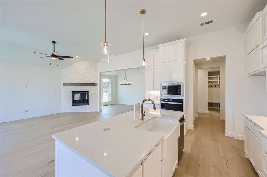 Kitchen with appliances with stainless steel finishes, ceiling fan with notable chandelier, a stone fireplace, decorative light fixtures, and a center island with sink