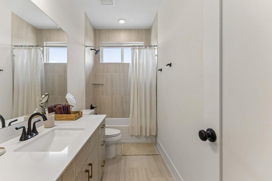 A modern bathroom features a clean white vanity countertop and neutral tiled tub surrounds.