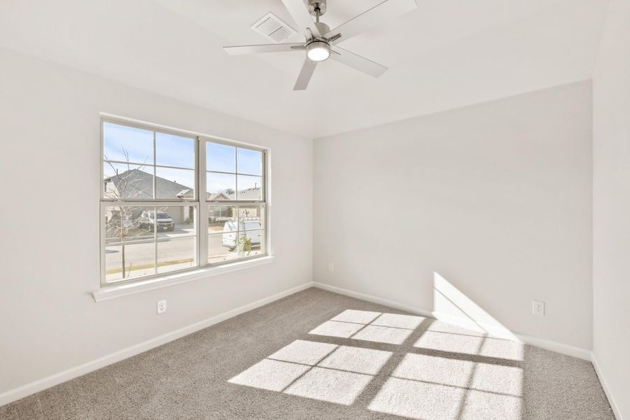 Empty bedroom with gray carpet, ceiling fan, and large window with neighborhood view Empty bedroom with gray carpet, ceiling fan, and large window with neighborhood view