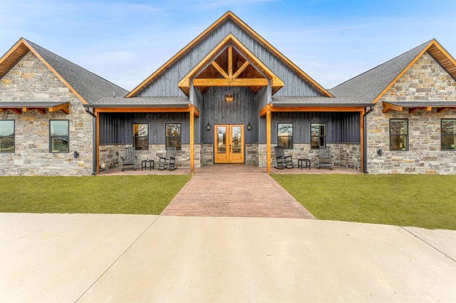 View of front of property with stone siding, a front yard, a porch, and french doors