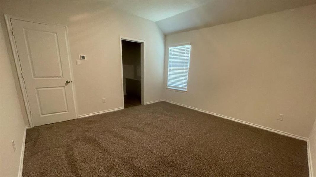 Carpeted room featuring a single window with blinds, a vaulted ceiling, and a white interior door Carpeted room featuring a single window with blinds, a vaulted ceiling, and a white interior door
