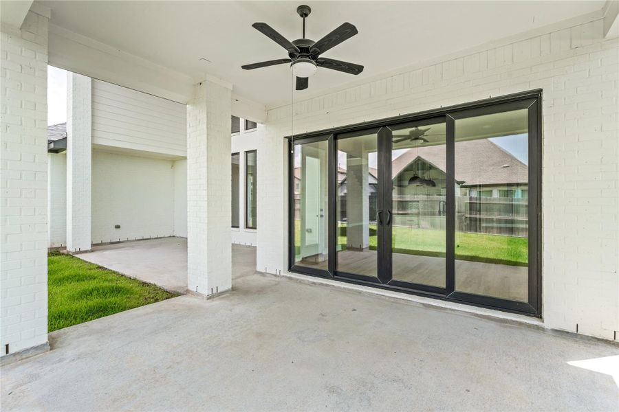 Spacious covered patio with modern ceiling fan and expansive sliding glass doors, perfect for seamless indoor-outdoor living.