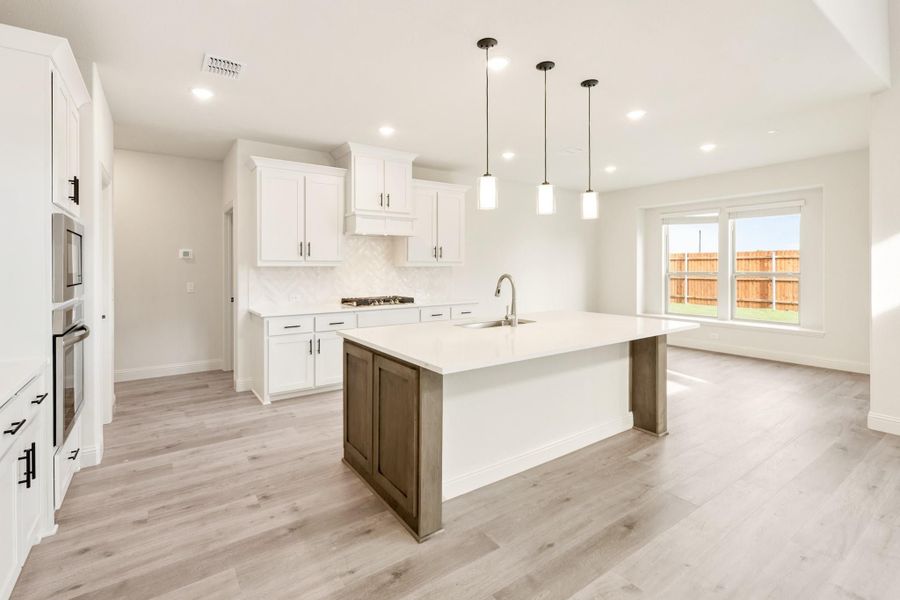 Open kitchen with white cabinets, large island with sink, pendant lights, and light wood floors Open kitchen with white cabinets, large island with sink, pendant lights, and light wood floors