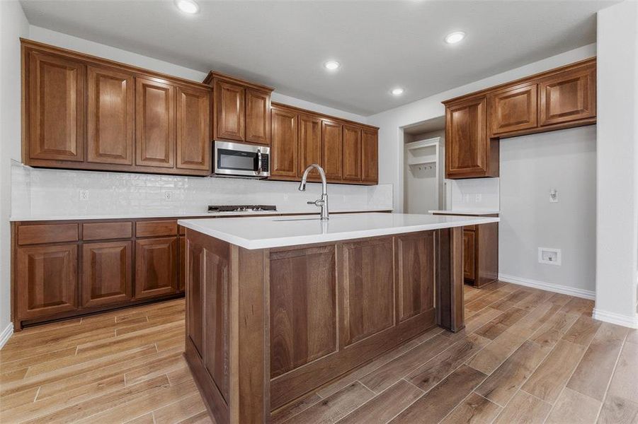 Kitchen with wood finish cabinets, wood tiled floors, decorative backsplash, a center island with sink, and stainless steel appliances