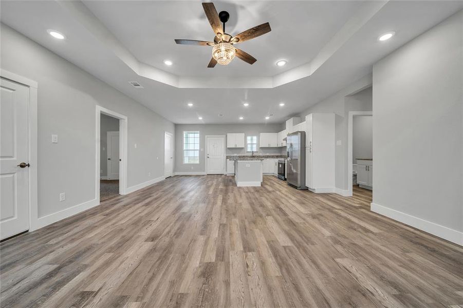 Unfurnished living room featuring ceiling fan, a raised ceiling, and light wood-type flooring