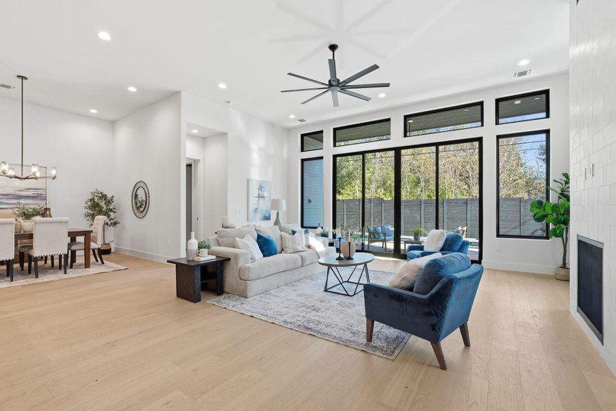 Living room with light wood-style floors, recessed lighting, ceiling fan, a fireplace, and a chandelier