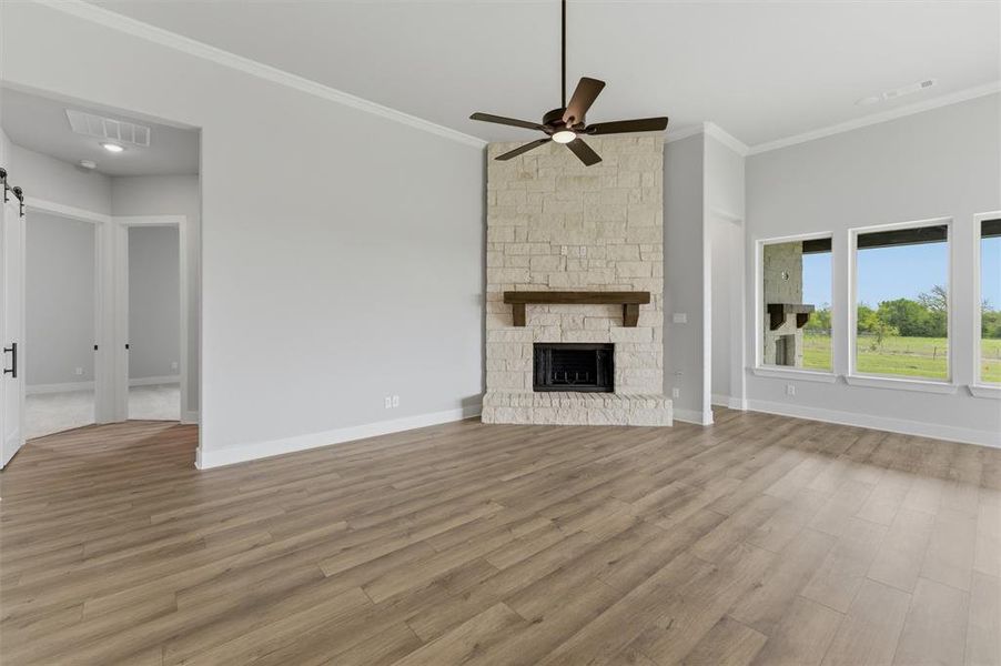 Unfurnished living room with light wood-style floors, a stone fireplace, a ceiling fan, and ornamental molding