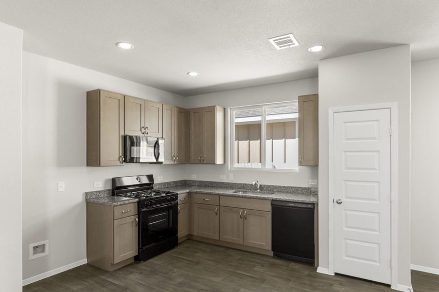 Image of an L-shaped kitchen with light brown cabinets, black appliances, granite countertops and a window above the sink