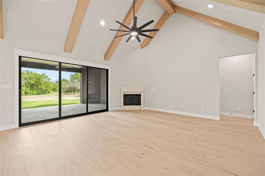 Unfurnished living room with high vaulted ceiling, beam ceiling, a fireplace, light wood finished floors, and recessed lighting Unfurnished living room with high vaulted ceiling, beam ceiling, a fireplace, light wood finished floors, and recessed lighting