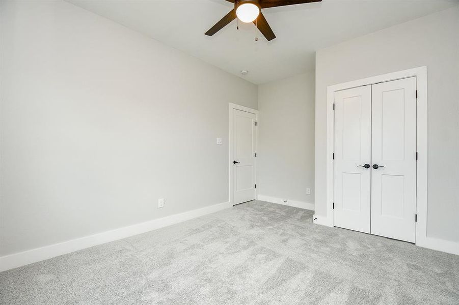 This is a clean, secondary bedroom featuring neutral walls, plush carpeting, a ceiling fan, and two white doors.