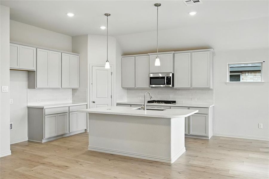 Kitchen featuring decorative light fixtures, tasteful backsplash, a kitchen island with sink, light wood finished floors, and recessed lighting Kitchen featuring decorative light fixtures, tasteful backsplash, a kitchen island with sink, light wood finished floors, and recessed lighting