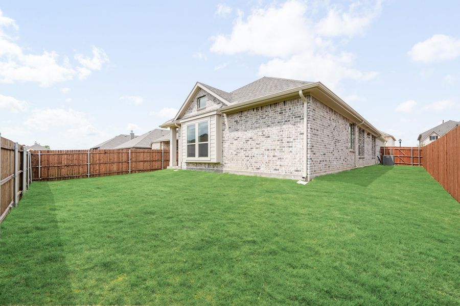 Backyard of single-story brick home with large green lawn and wood privacy fence