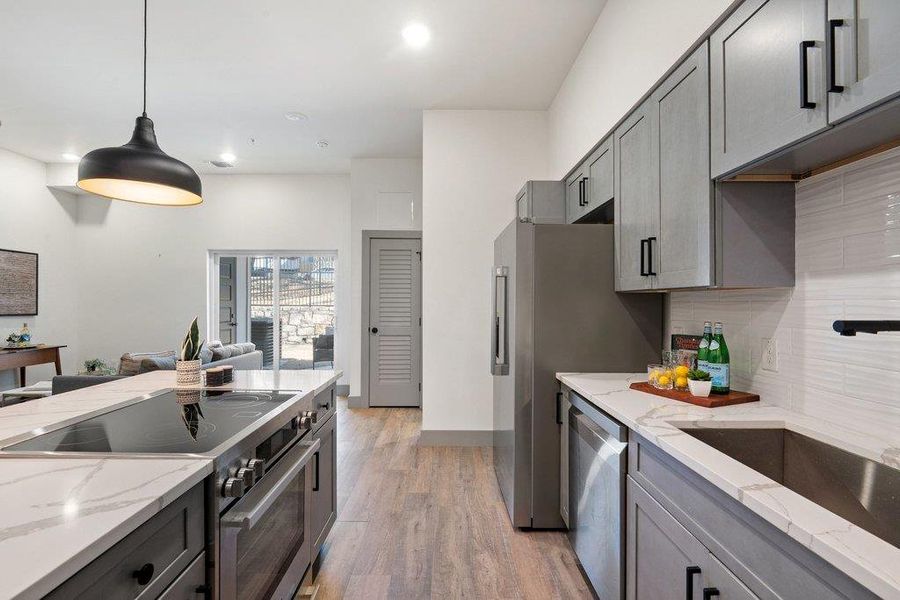 Kitchen with stainless steel appliances, light stone countertops, gray cabinetry, and decorative light fixtures
