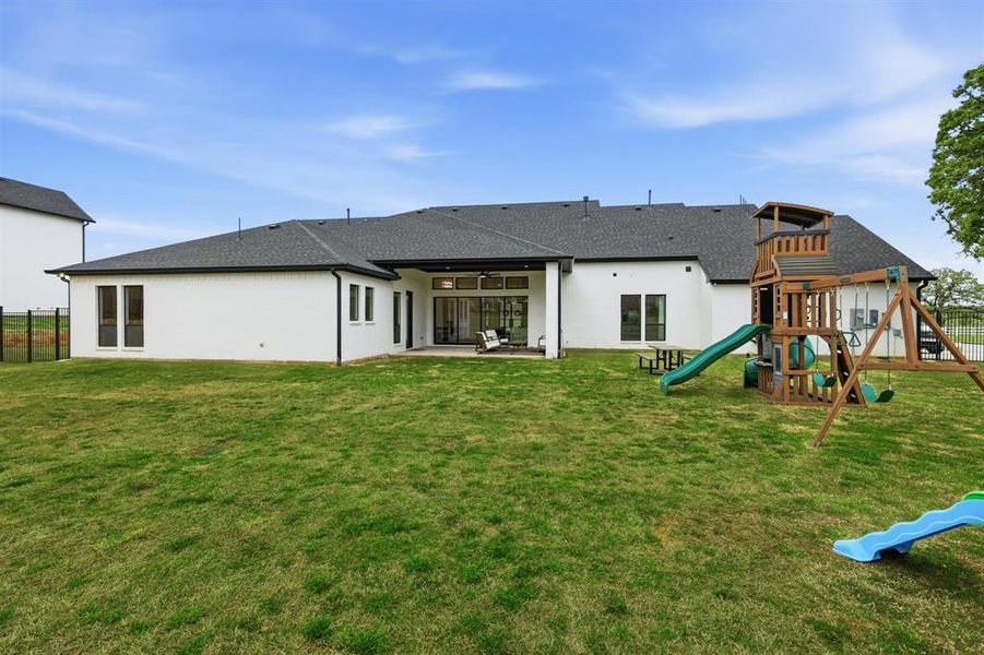 Rear view of house with a patio, a playground, stucco siding, and roof with shingles