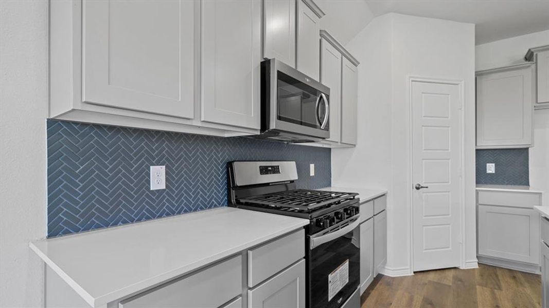 Kitchen featuring appliances with stainless steel finishes, backsplash, dark wood finished floors, gray cabinetry, and light stone counters