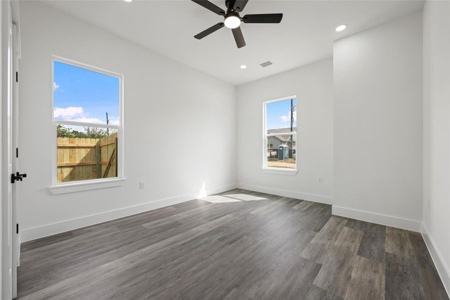 Spacious room featuring wood-finish flooring, crisp white walls, and a contemporary ceiling fan
