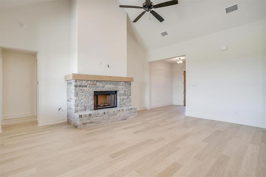 Unfurnished living room with light hardwood / wood-style floors, a fireplace, high vaulted ceiling, and ceiling fan