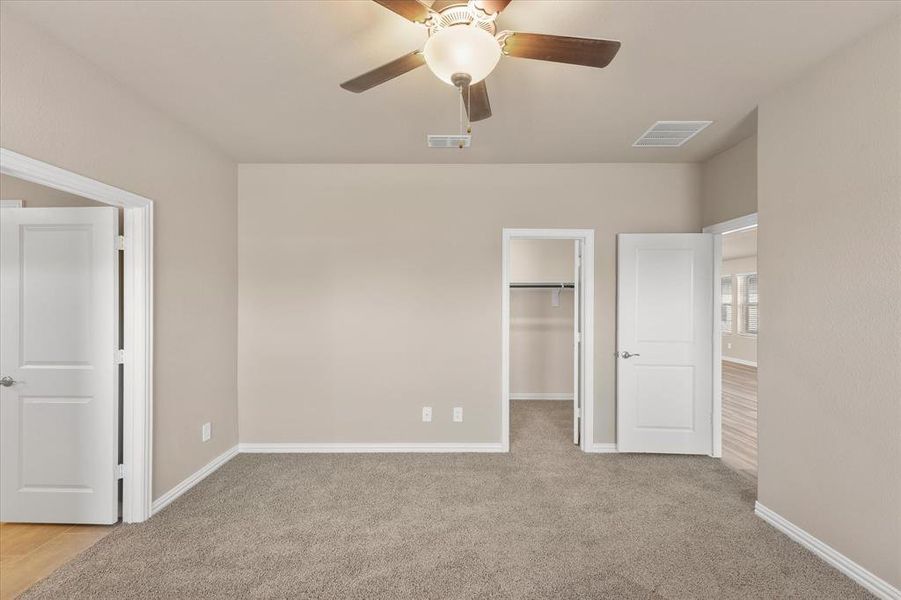 Unfurnished bedroom featuring a spacious closet, light colored carpet, and ceiling fan Unfurnished bedroom featuring a spacious closet, light colored carpet, and ceiling fan