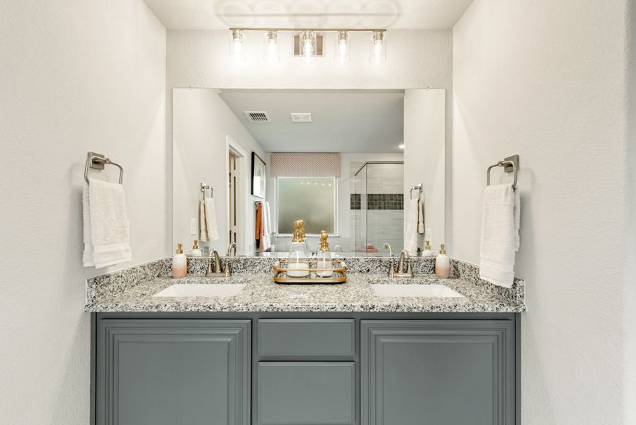 Bathroom double vanity with gray cabinets, granite countertop, two sinks, and large mirror with overhead lighting