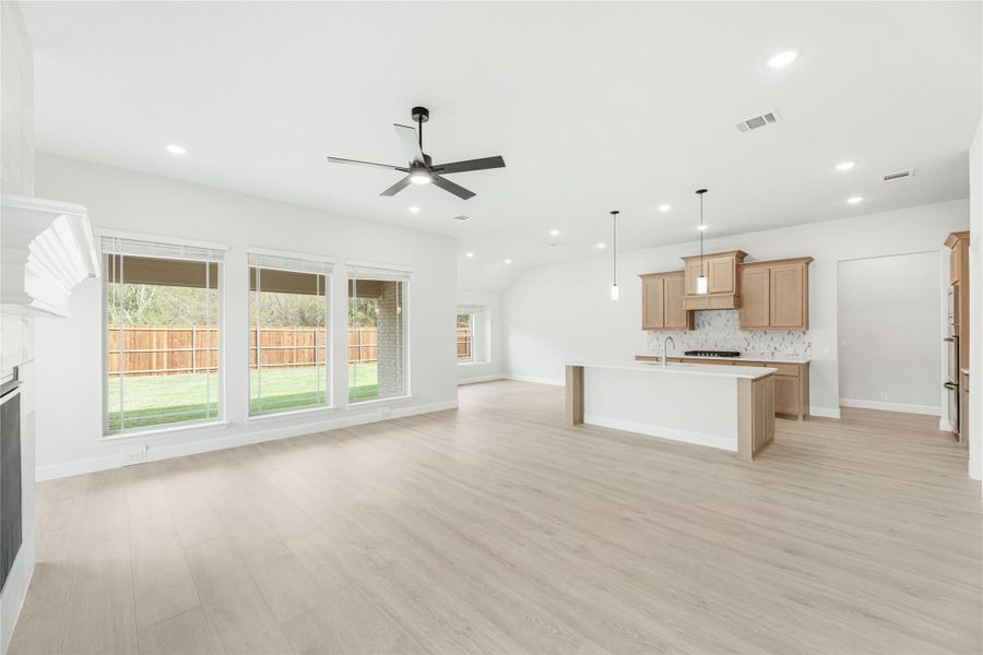 Open-concept living area with light wood floors, ceiling fan, and kitchen with island and wood cabinets in background