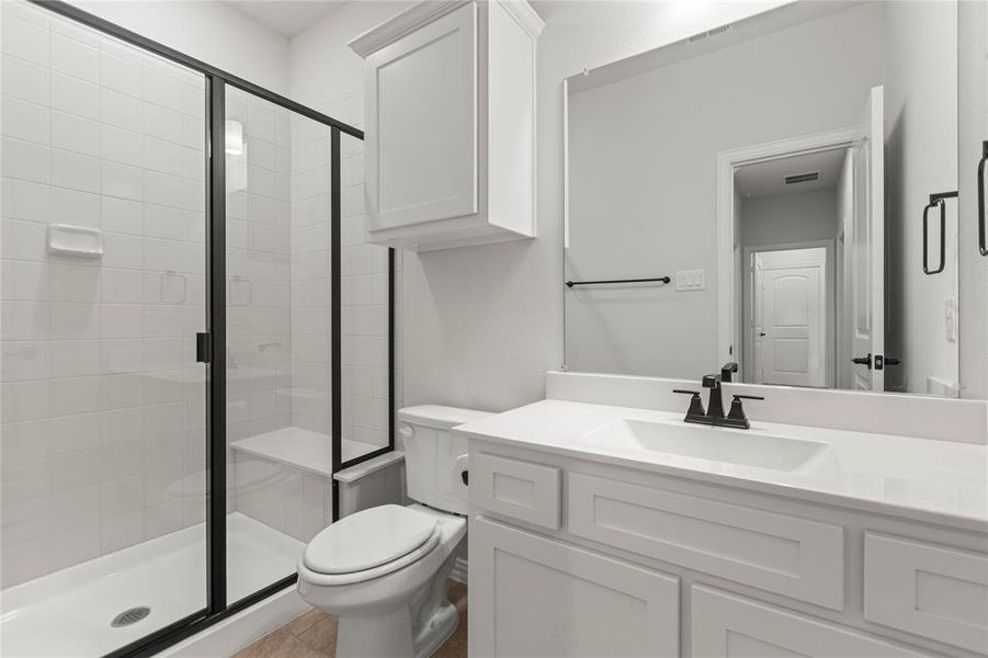 Bathroom with a shower with shower door, vanity, tile patterned floors, and toilet