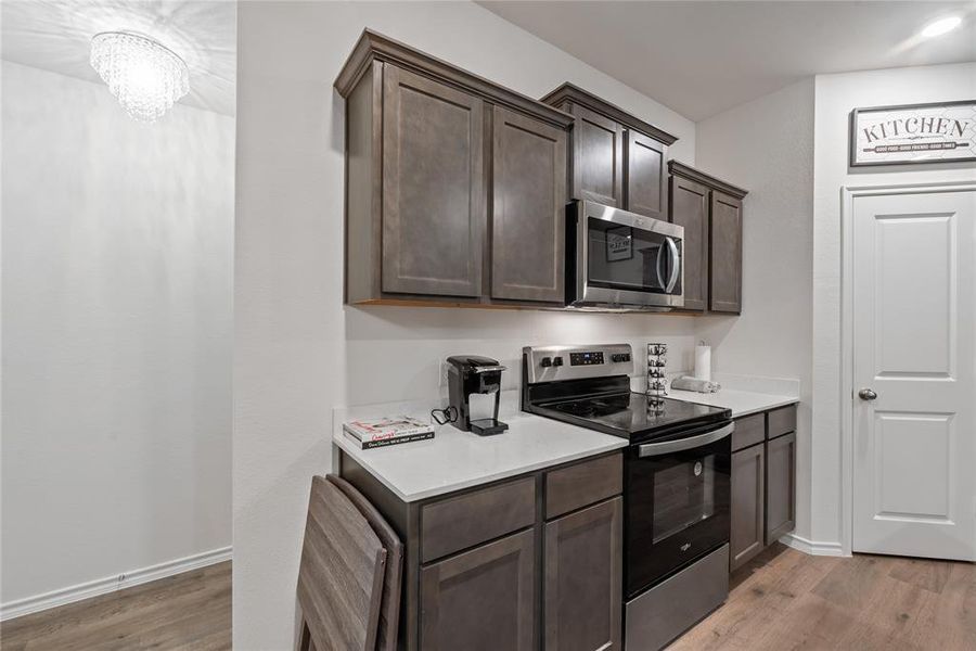 Kitchen with stainless steel appliances, dark brown cabinetry, light wood-style flooring, and light stone counters