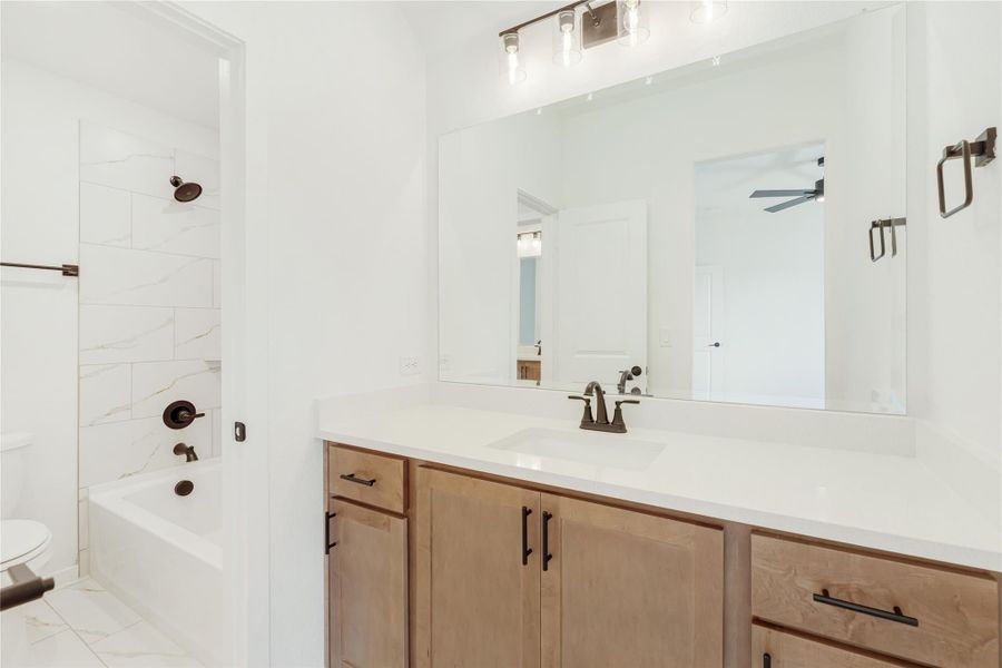 Bathroom with wood vanity, white countertop, large mirror, and tiled tub-shower combo with dark bronze fixtures