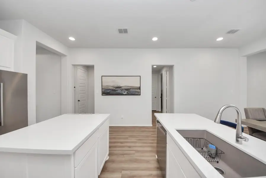 This photo showcases a modern kitchen with sleek white cabinetry and countertops, a stainless steel sink, and wood flooring. Recessed lighting and neutral walls create a bright, open atmosphere.