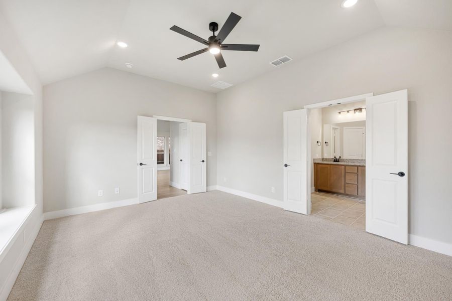 Spacious master bedroom with carpet, vaulted ceiling, ceiling fan, and open ensuite bathroom doorway